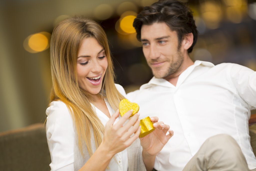 A woman receiving an engagement diamond in a small, heart-shaped box