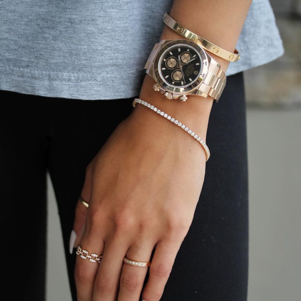 A woman wearing a thin, diamond bracelet with a few rings and a men's watch